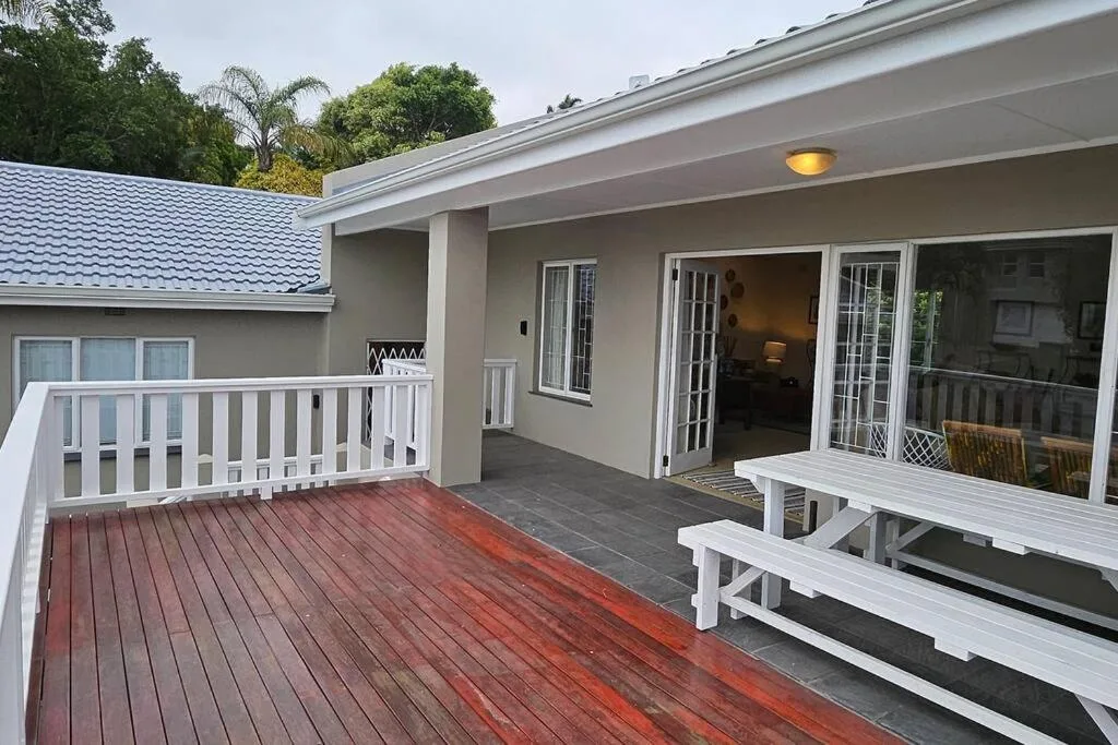 Spacious wooden deck with white benches and garden views