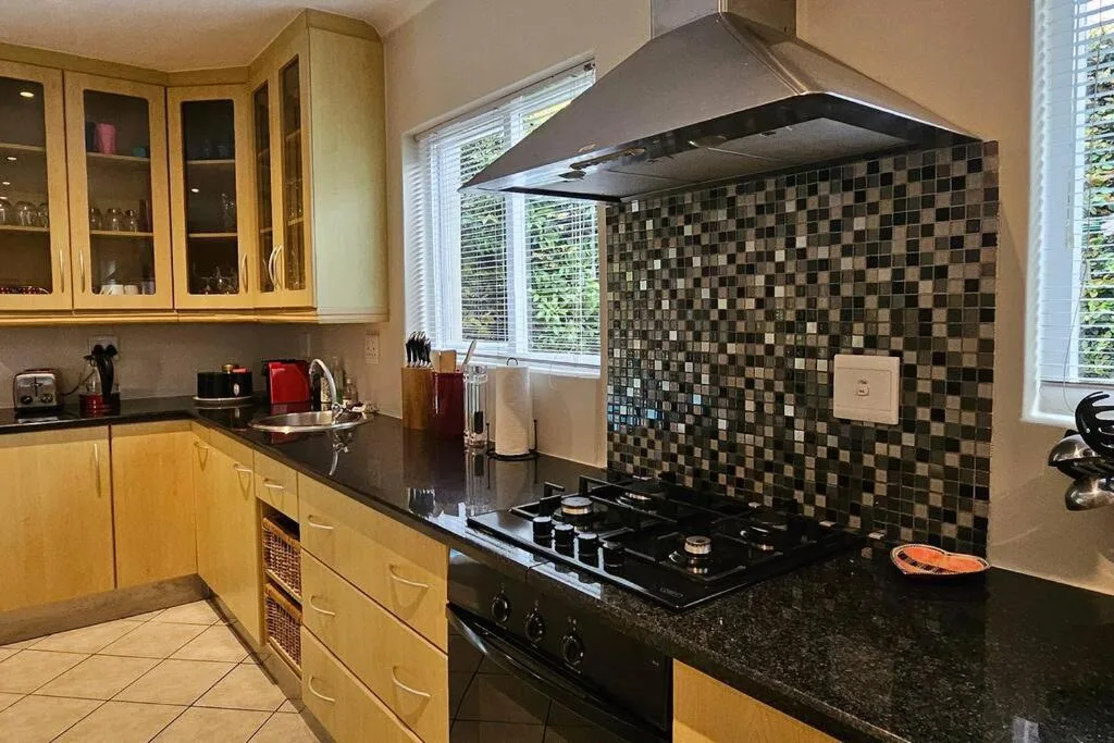Modern kitchen with wooden cabinetry, black granite counters, gas cooktop, and mosaic backsplash