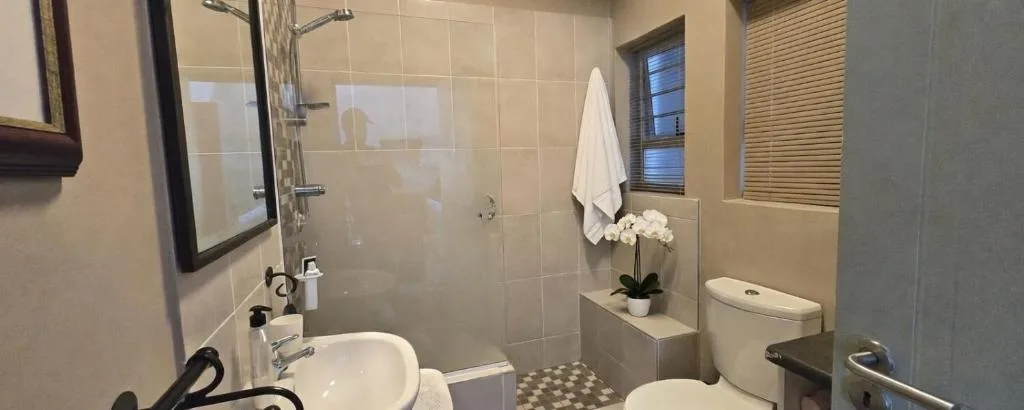 Clean bathroom with sink, toilet, shower enclosure, and white flowers