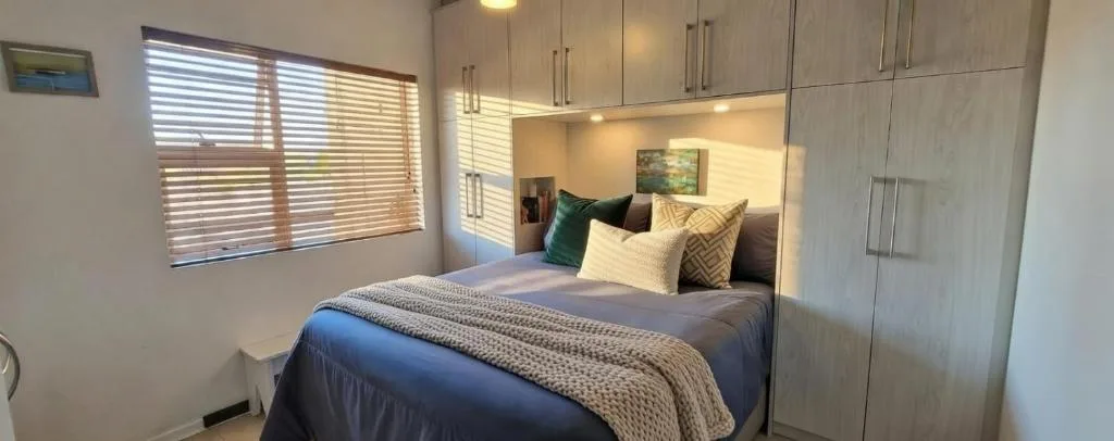 Modern bedroom with queen bed, built-in wardrobes, and natural light from window