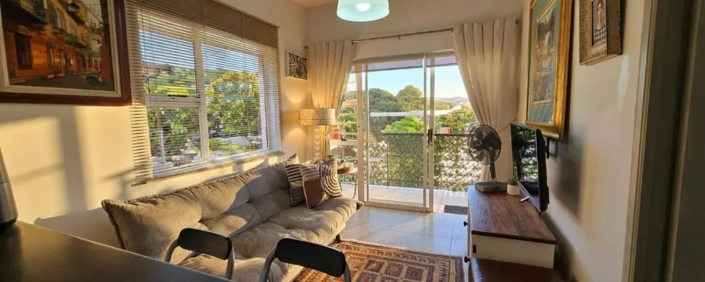 Bright lounge with sofa, TV, and scenic garden views through glass doors