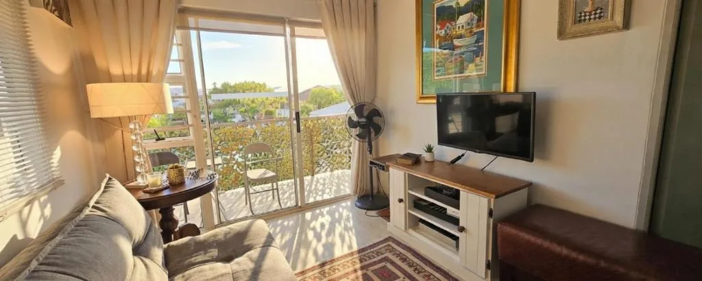 Bright lounge with TV, sofa, and scenic lagoon views through glass doors