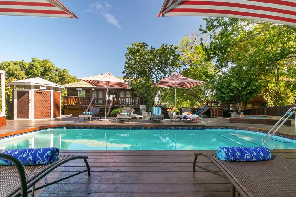 Crystal clear swimming pool with wooden deck, loungers, and red striped umbrellas