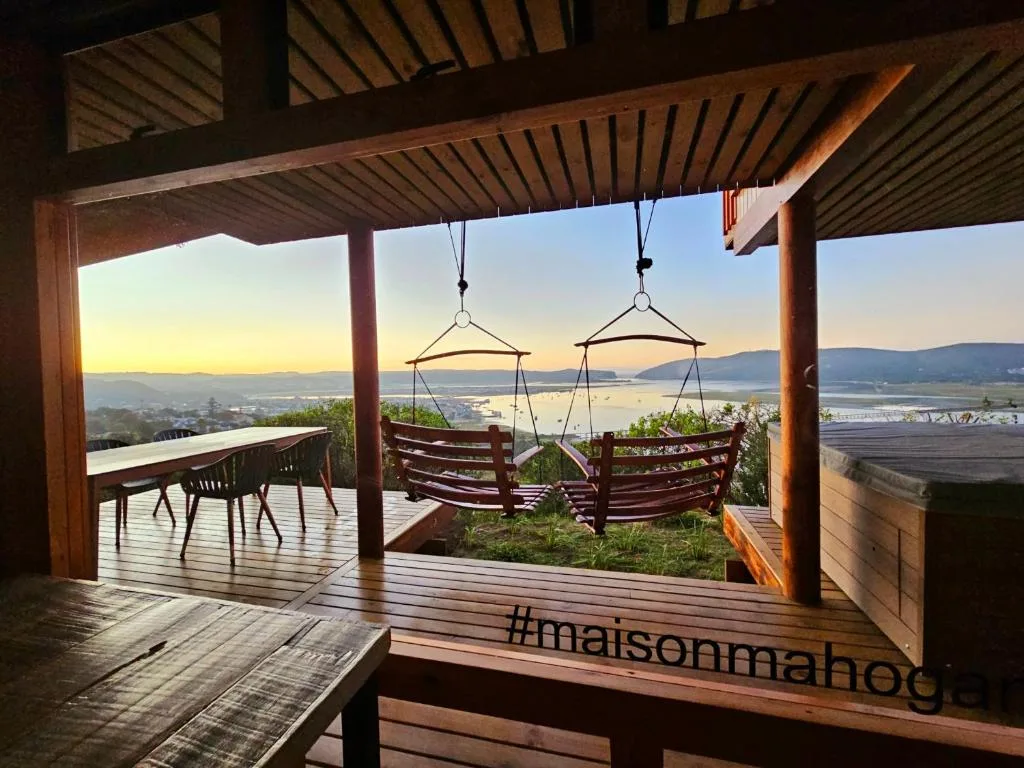 Wooden deck with pergola, hanging swings, and panoramic lagoon views at sunset