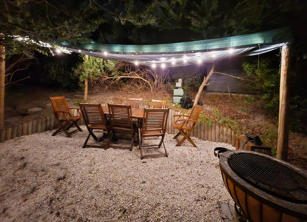 Illuminated outdoor seating area with wooden chairs and fire pit at night
