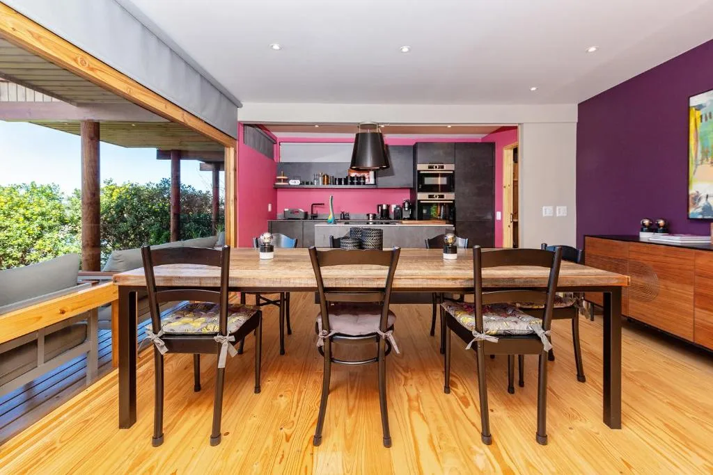 Open-plan dining area with wooden table and chairs, adjacent kitchen with pink cabinetry