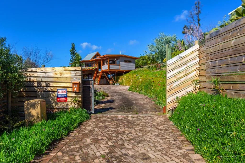 Modern elevated wooden house with brick driveway and manicured hedges
