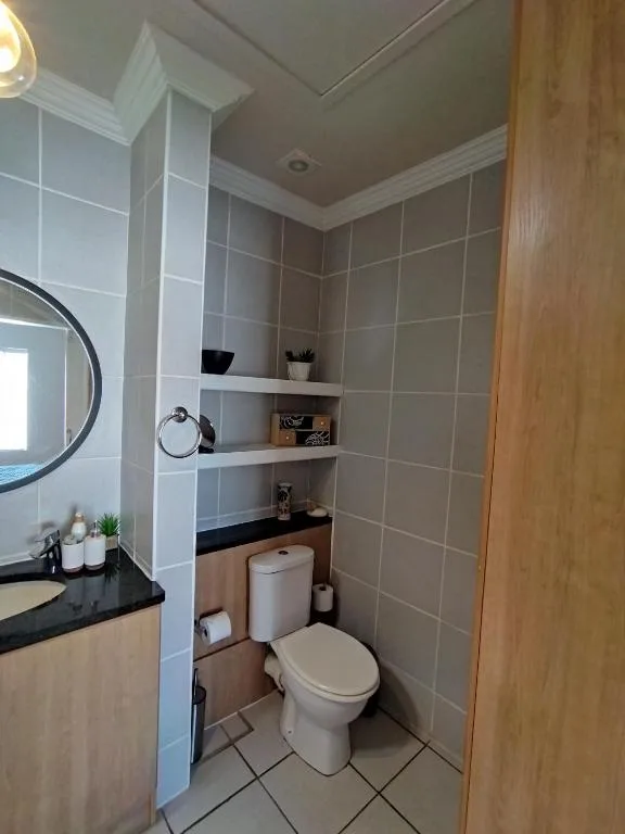 Modern bathroom with tiled walls, vanity sink, toilet, and storage shelves
