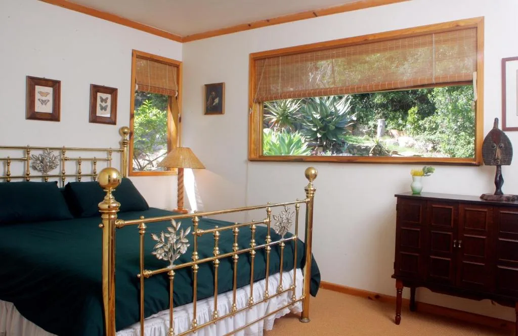 Bedroom with brass bed frame, green bedding, wooden dresser, and garden views