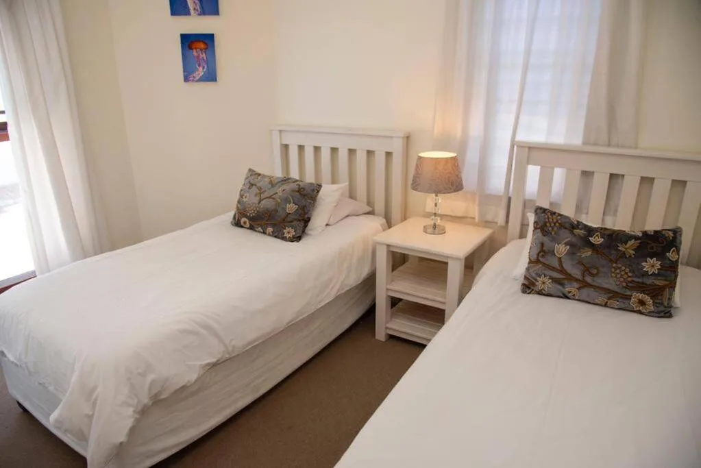 Twin bedroom with white beds, decorative pillows, and bedside lamp