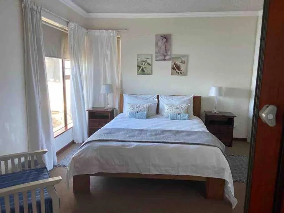 Bright bedroom with double bed, wooden nightstands, and garden views through curtained doors