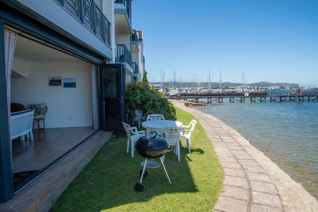 Waterfront patio with braai, white chairs, and marina views beyond