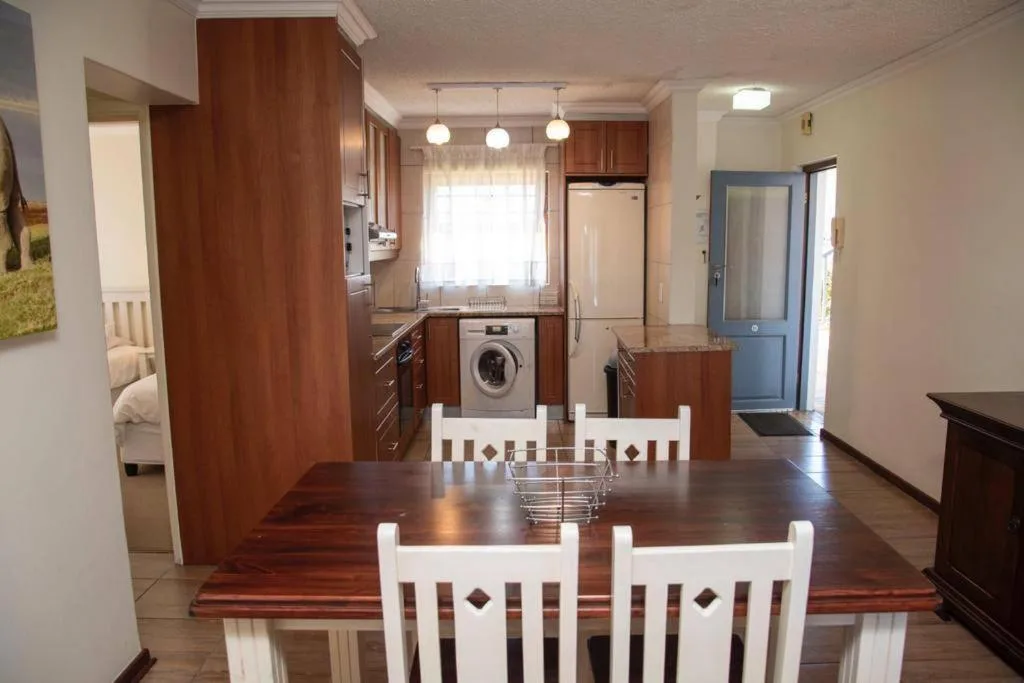 Dining area with wooden table and white chairs overlooking kitchen