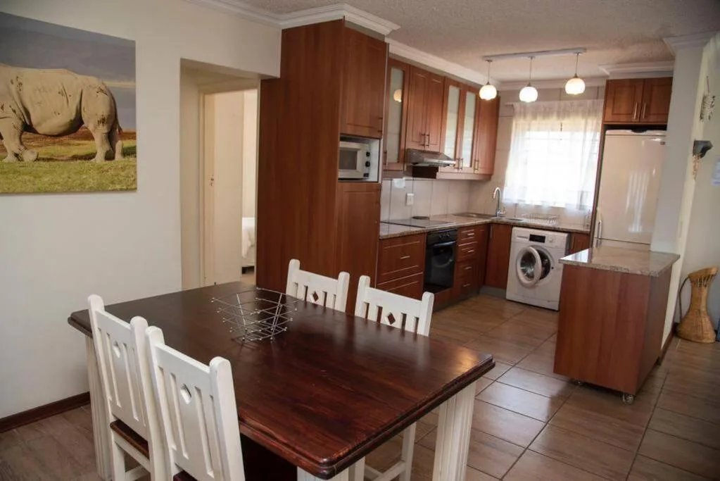 Spacious dining area with wooden table and white chairs, adjacent kitchen
