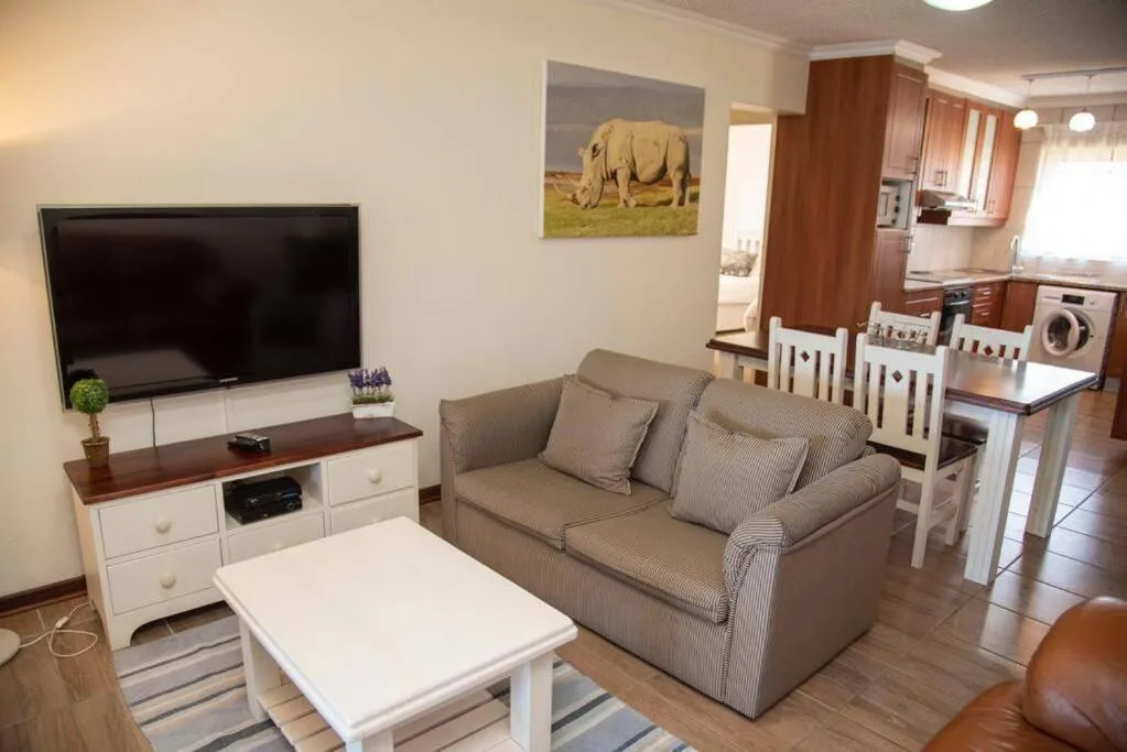 Open-plan lounge with sofa, TV, and kitchen area visible beyond