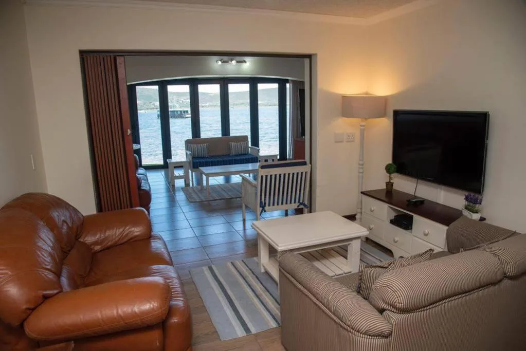 Spacious lounge with leather chair, sofa, TV, and water views through glass doors
