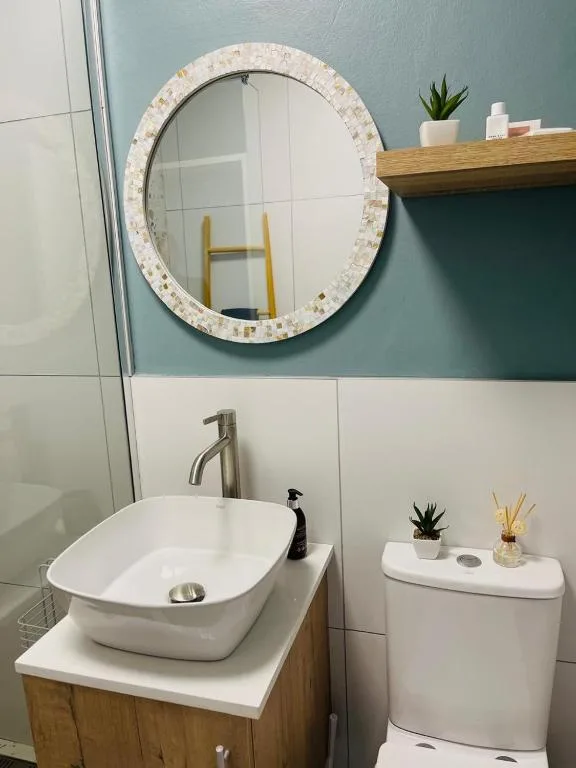 Modern bathroom with round mirror, vessel sink, and teal accent wall