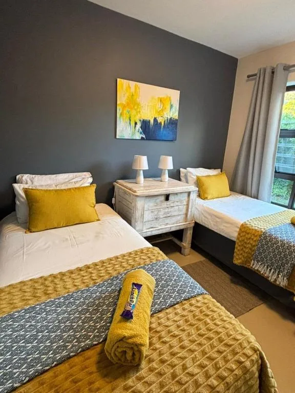 Twin bedroom with yellow accents, shared nightstand, and dark accent wall