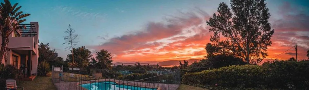 Dramatic sunset sky above Knysna town with pool and garden foreground