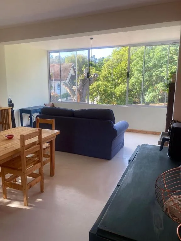 Spacious lounge with dark sofa, wooden dining table, and large windows overlooking trees