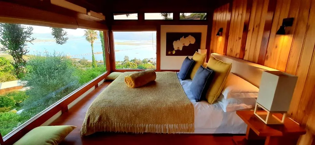 Spacious bedroom with water views, wooden beams, and colorful accent pillows
