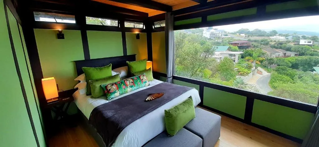Modern bedroom with green walls, queen bed, and expansive lagoon views through large windows