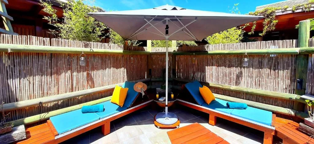 Wooden deck with blue loungers, umbrella, and colorful cushions