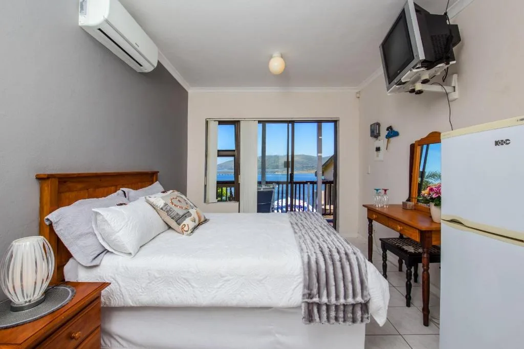 Bright bedroom with wooden bed, white linens, and lagoon views through glass doors