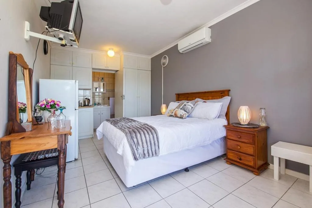 Spacious bedroom with queen bed, wooden furniture, and kitchenette in background
