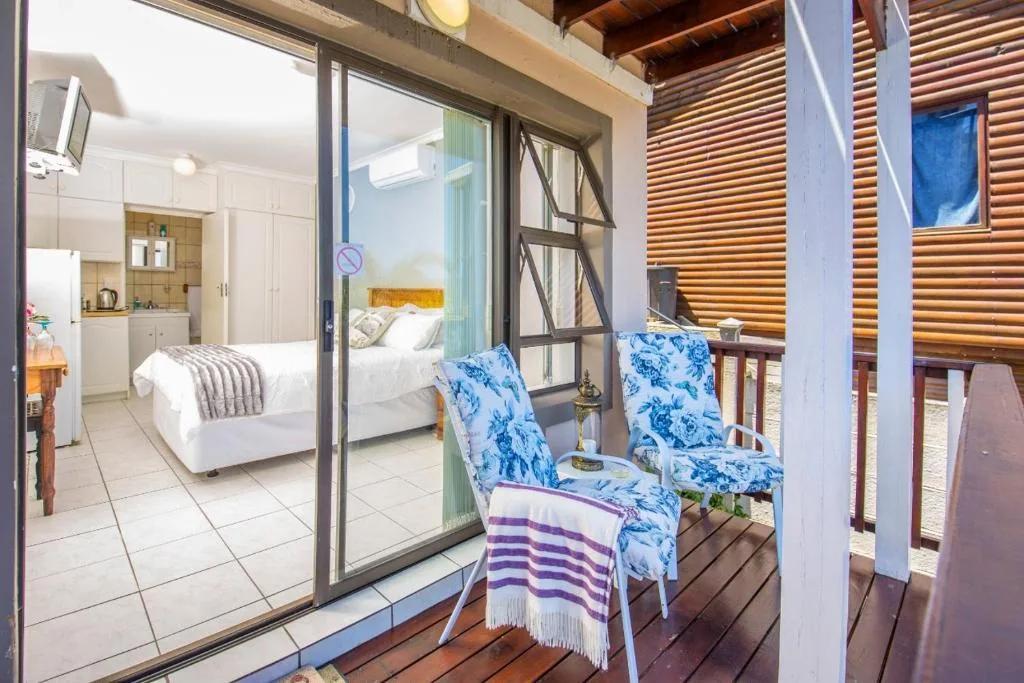 Wooden deck with blue patterned chairs overlooking bedroom interior