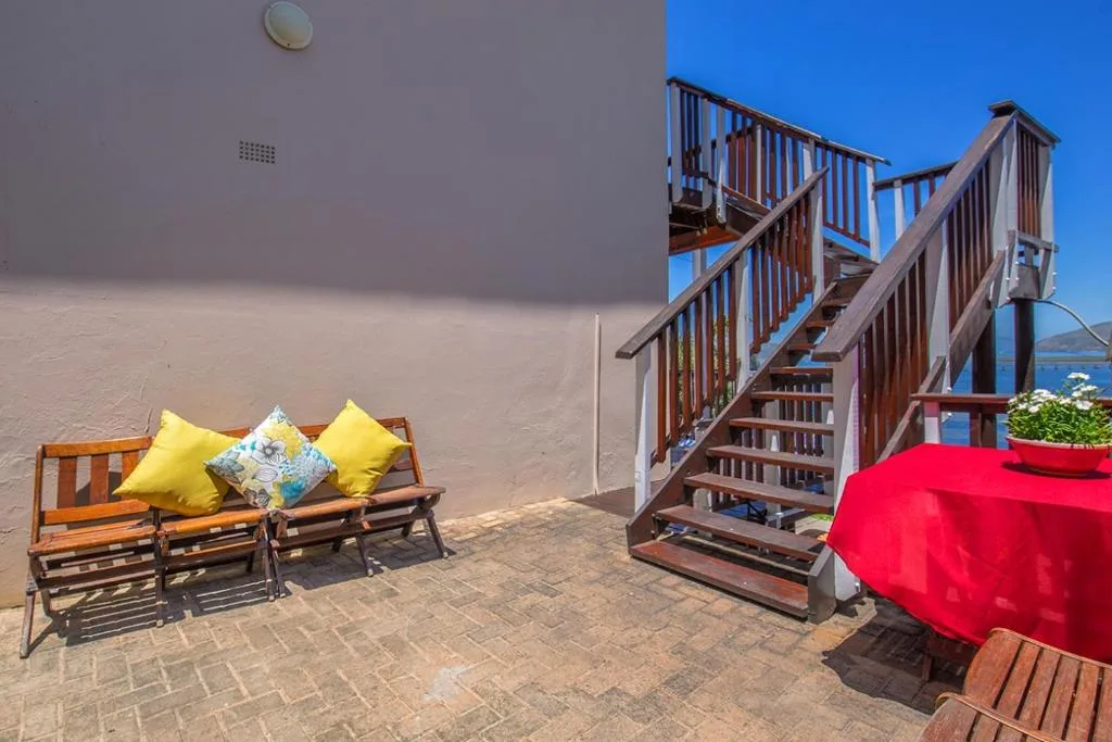 Sunny outdoor patio with wooden bench, yellow cushions, and ocean view stairs