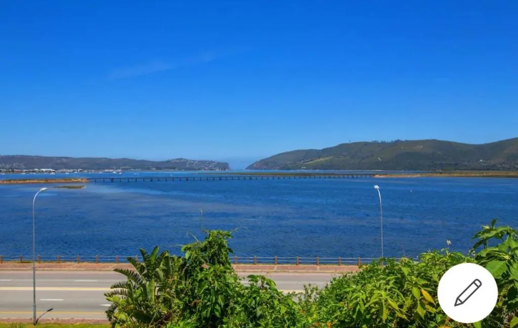 Scenic blue lagoon with bridge and green hills under clear sky