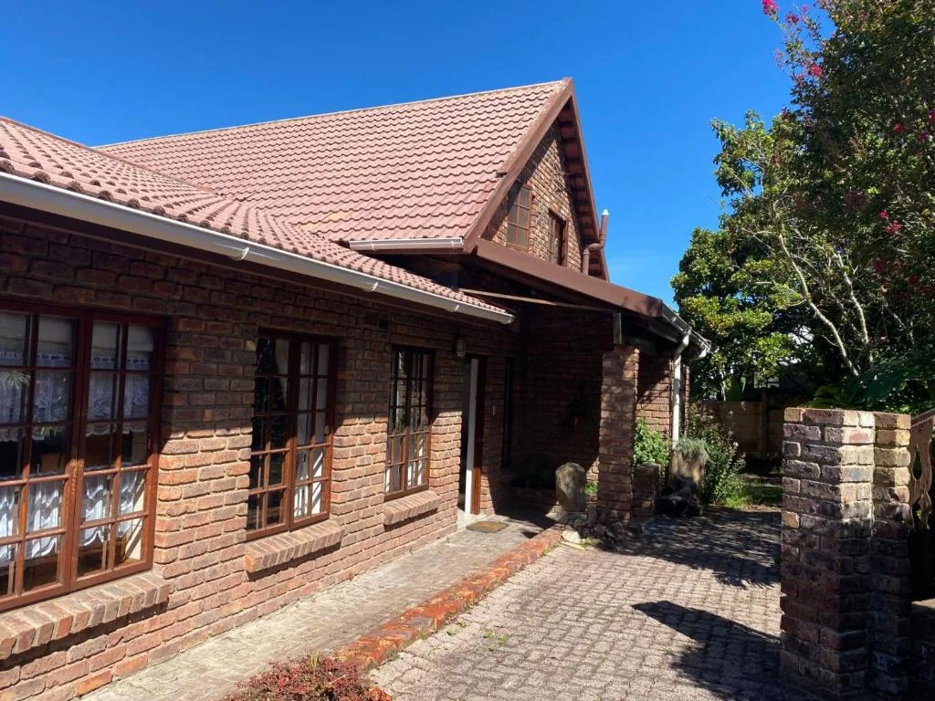 Red brick cottage with terracotta tile roof and paved driveway entrance