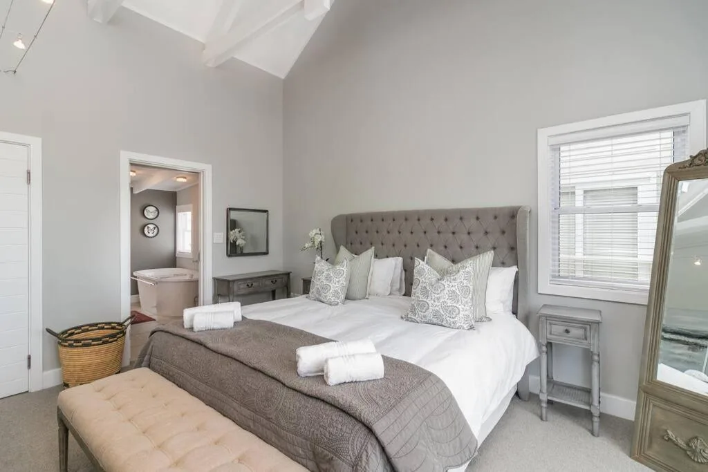 Spacious bedroom with gray upholstered bed, white bedding, and ensuite bathroom access