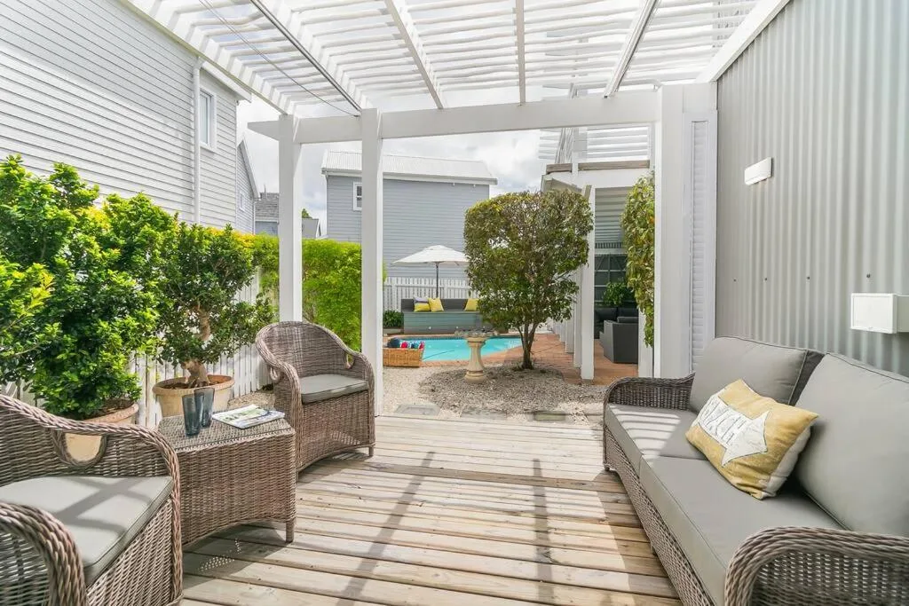Covered patio with wicker seating, wooden deck, and pool view beyond