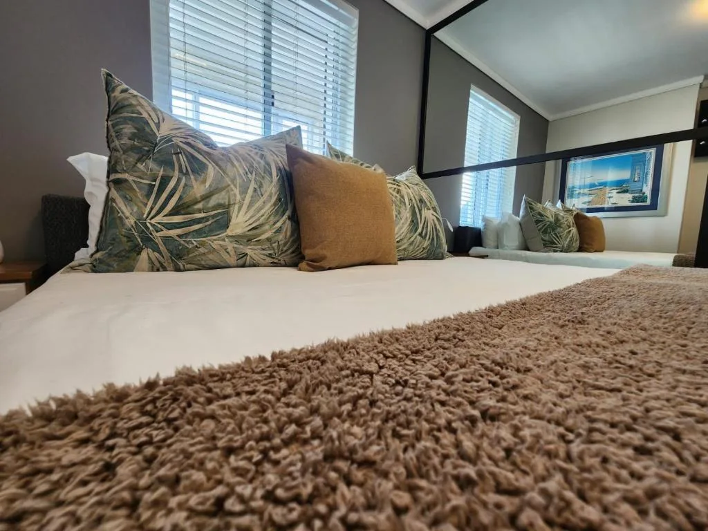 Comfortable bed with tropical patterned pillows and neutral bedding in bright room