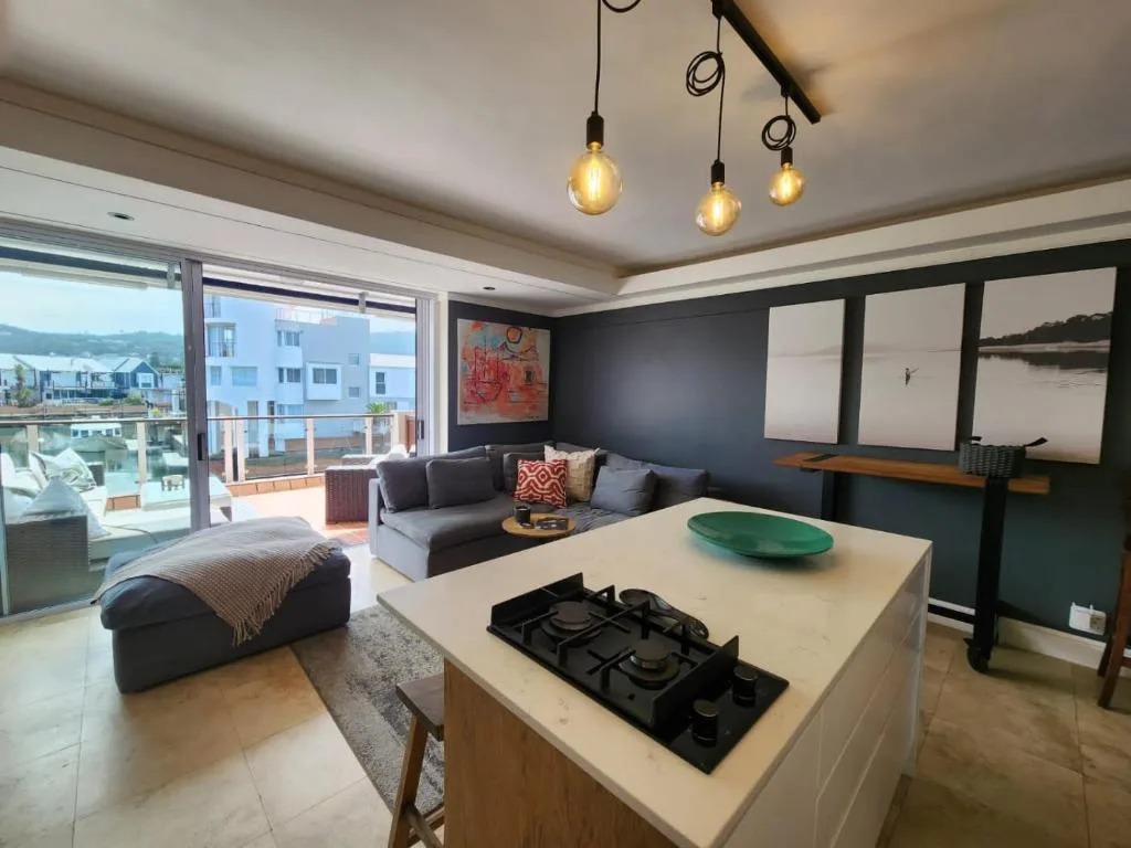 Modern open-plan lounge with dark accent wall, sofa, pendant lighting, and waterfront views