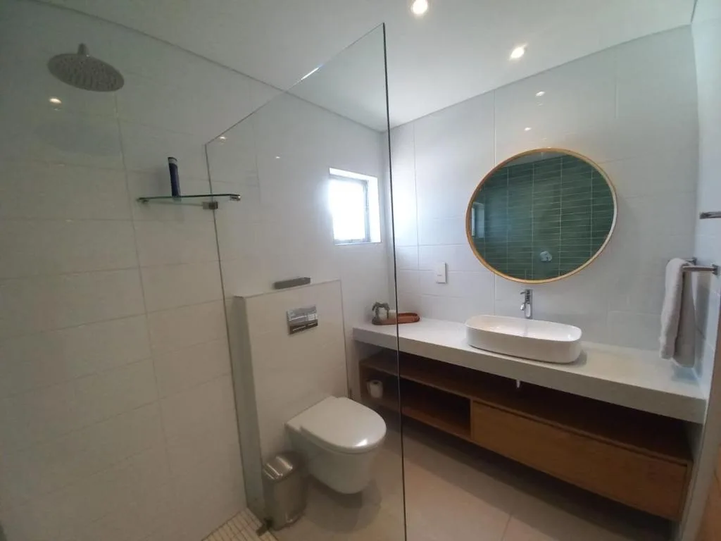 Modern bathroom with walk-in shower, round mirror, and white vanity sink