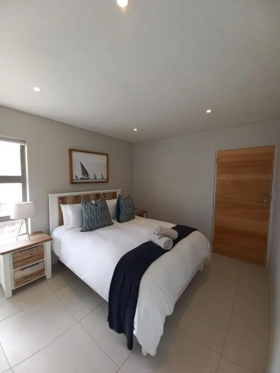Bright bedroom with queen bed, wooden nightstand, and nautical wall art