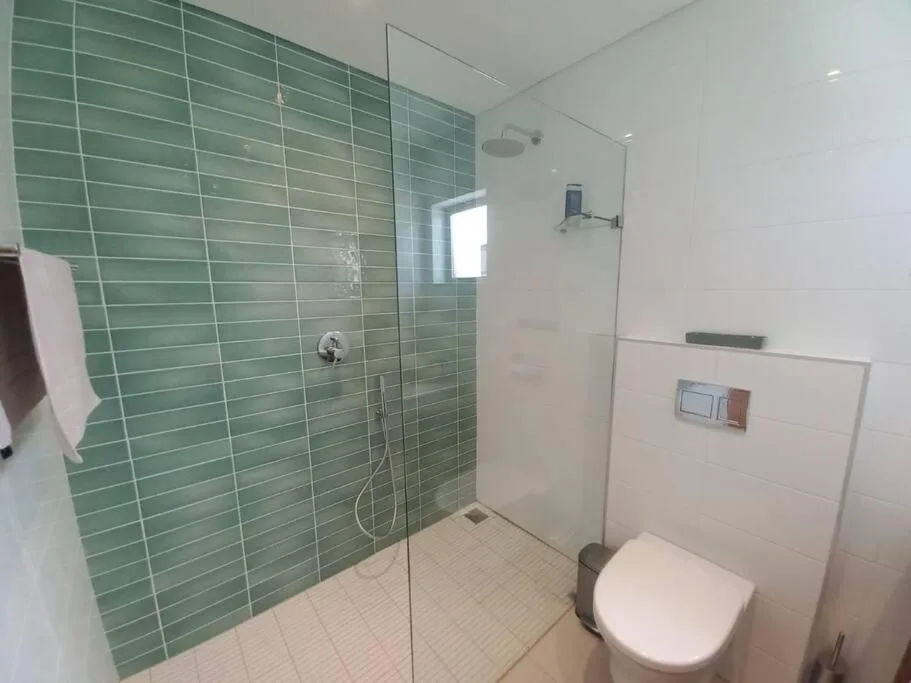Modern bathroom with green tile shower enclosure and white toilet