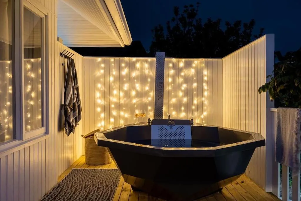 Illuminated outdoor bathtub on wooden deck with warm string lights