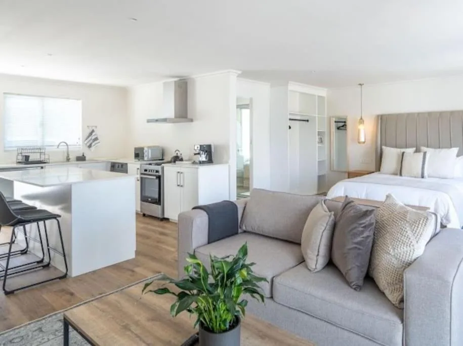 Modern open-plan lounge with gray sofa, kitchen and bedroom visible
