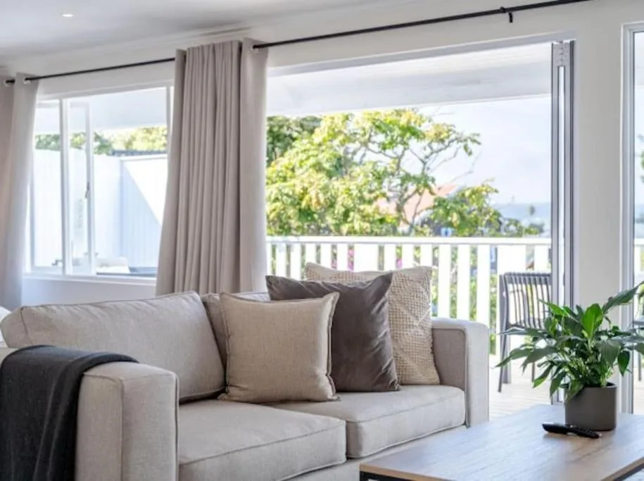 Bright lounge with beige sofa overlooking lagoon and tree through glass doors