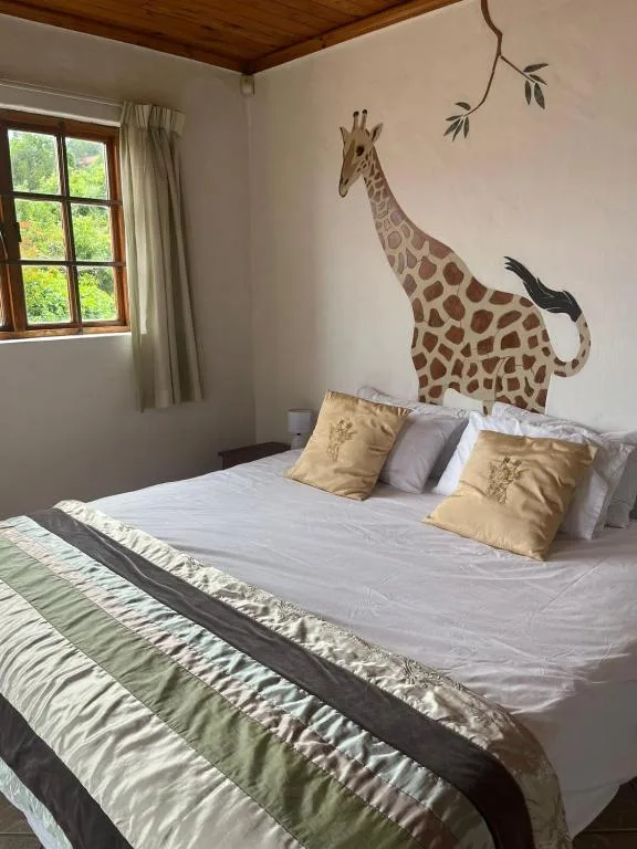 Bedroom with giraffe mural, white bedding, gold pillows, and garden views