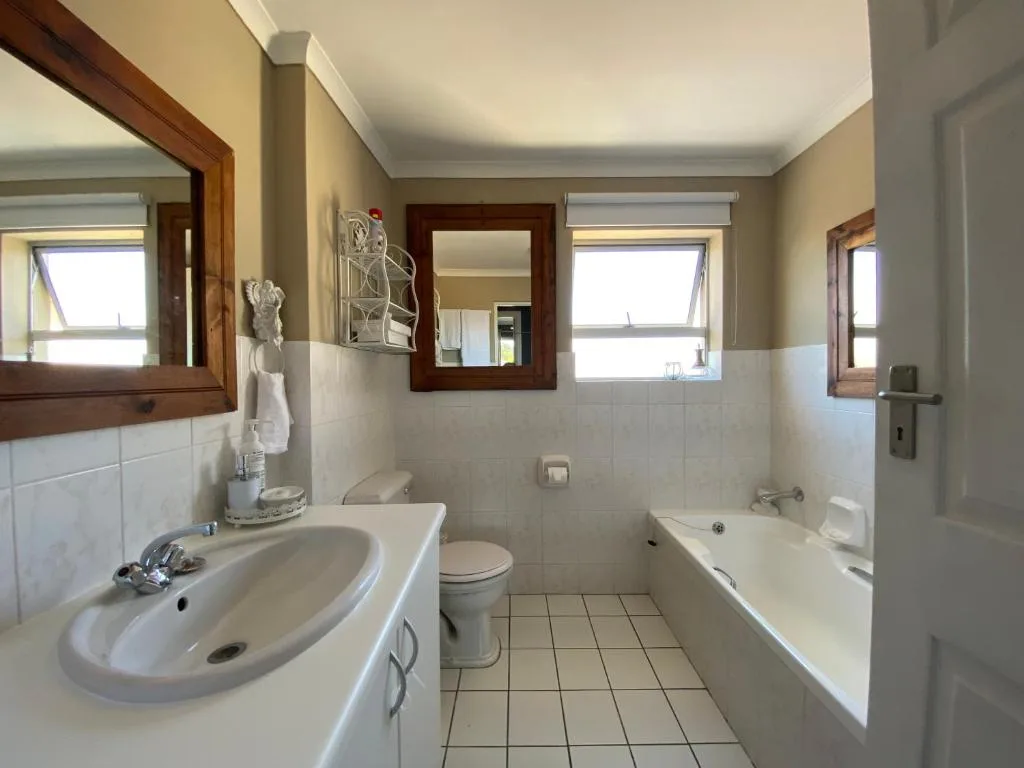 Bright bathroom with basin, toilet, bathtub, and wooden-framed mirror