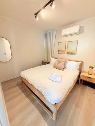 Bright modern bedroom with queen bed, white bedding, and wall-mounted air conditioning unit