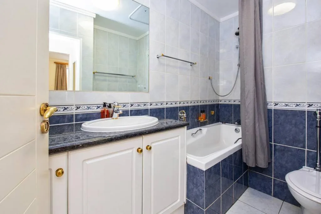 Modern bathroom with white vanity, dark blue tile accents, bathtub and shower