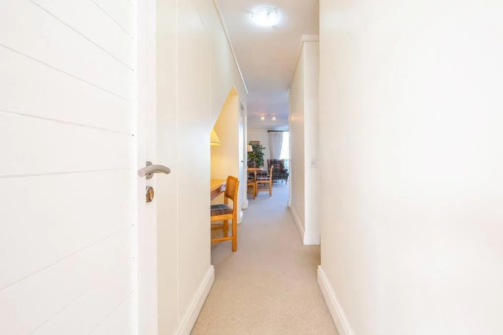 Bright hallway with wooden chairs and neutral carpeting, leading to living area