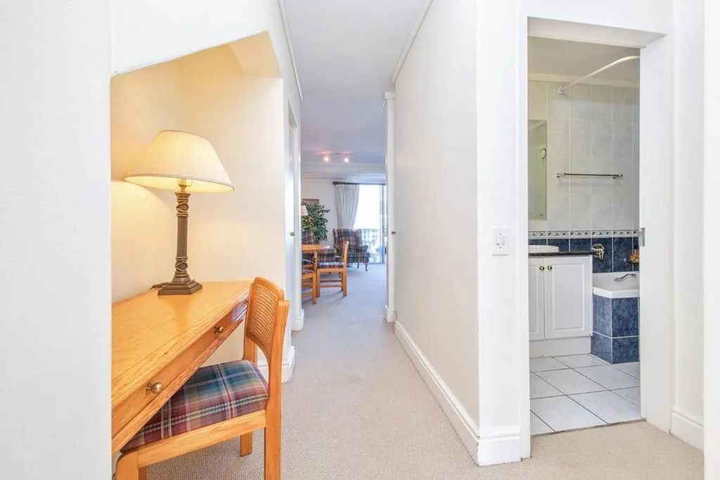 Hallway view with desk, lamp, and bathroom entrance doorway