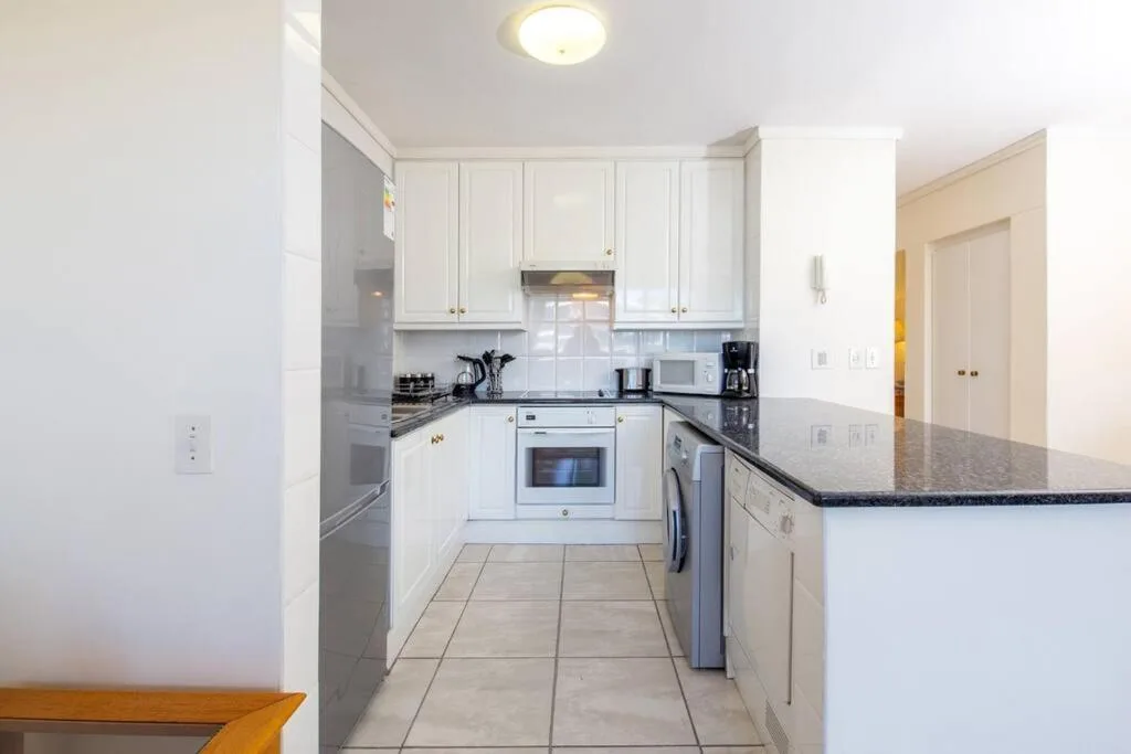 Modern white kitchen with granite countertops, stainless steel appliances, and tile flooring